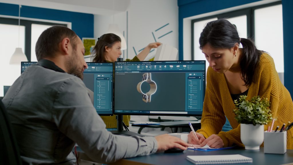 Team discussing about industrial project using dual monitors setup to desing 3D gears and metalic clamp in CAD software. Industrial engineer and african project manager working together in creative office
